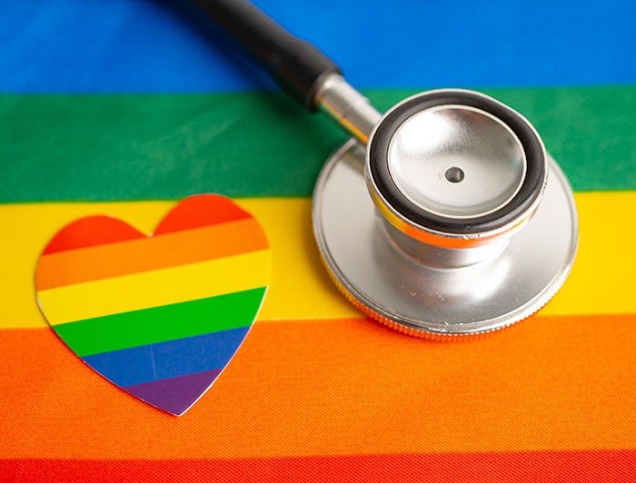 stethoscope placed on a LGBTQ+ flag with a LGBTQ+ themed heart sticker next to the stethoscope