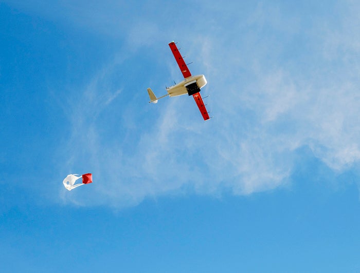 Zipline drone flies across blue sky trailing a small red package