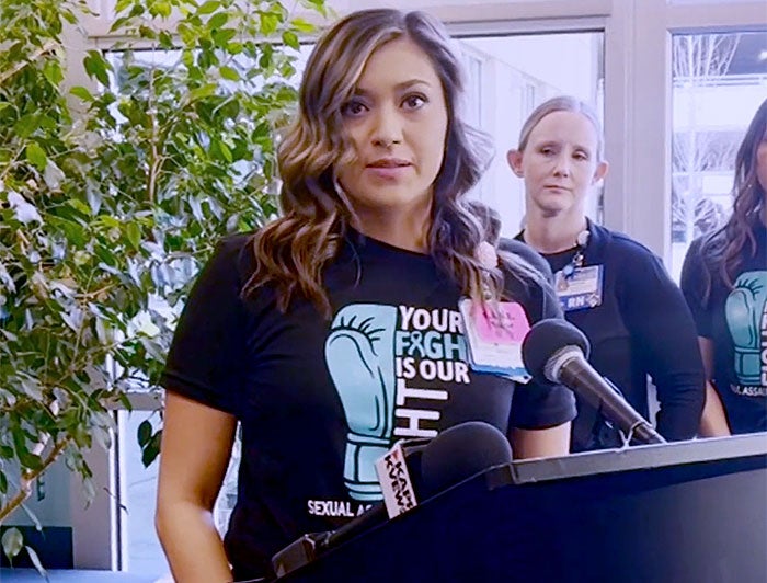 NWoman stands at podium wearing tee that reads Your Fight is Our Fight
