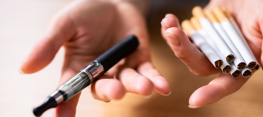 A person holds a nicotine vape in one hand and multiple cigarettes in the other