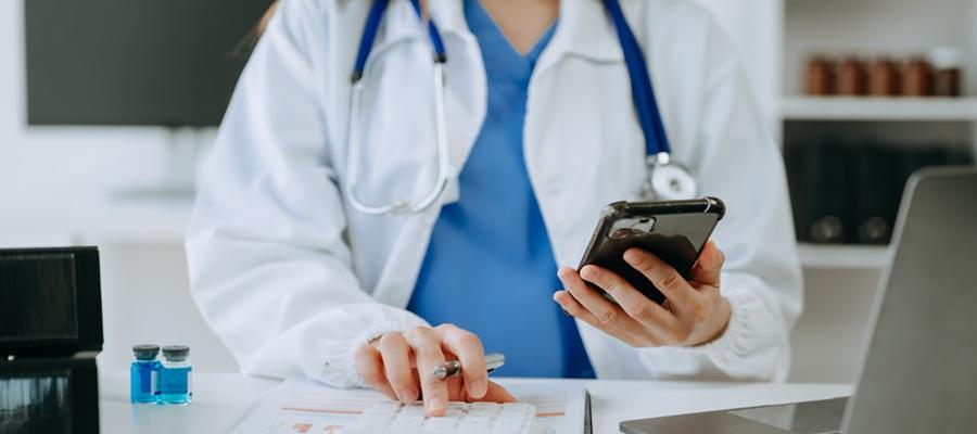 Clinician uses smartphone and laptop, reads data from sheet of paper.